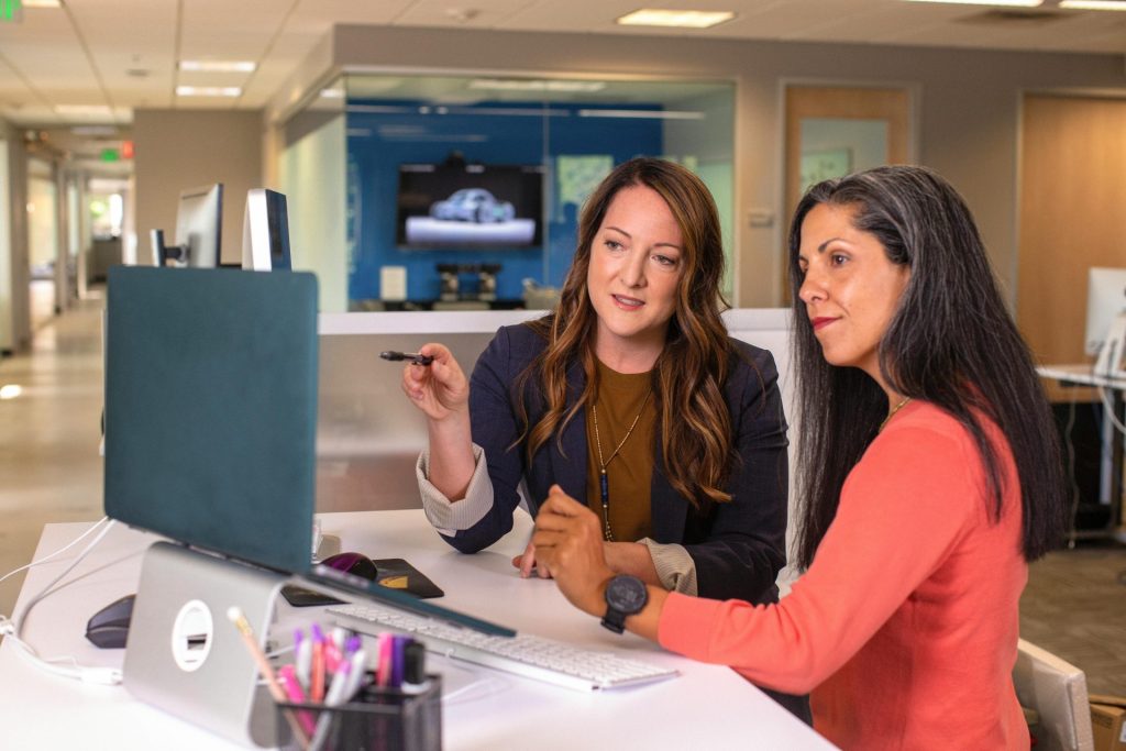 Deux femmes professionnelles discutent ensemble des détails d'un projet dans un environnement de bureau moderne.
