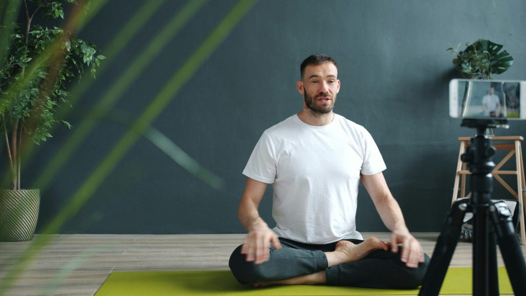 Un homme médite sur un tapis de yoga et se filme avec son téléphone.