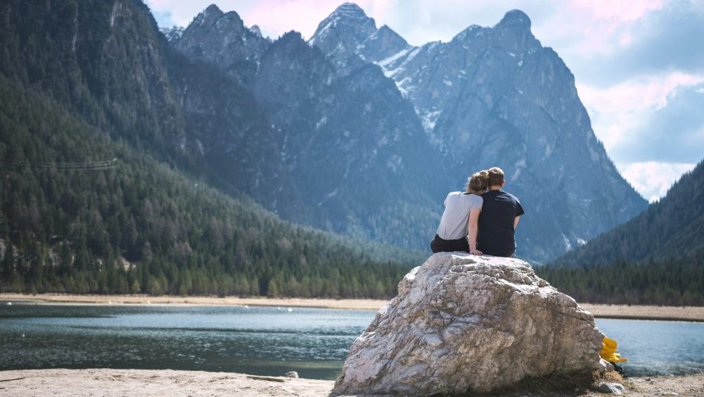 Un couple est assis sur un rocher, contemplant un lac.