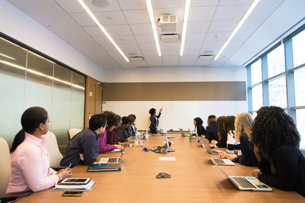 Des personnes assises autour d'une table de conférence regardent une femme qui parle.
